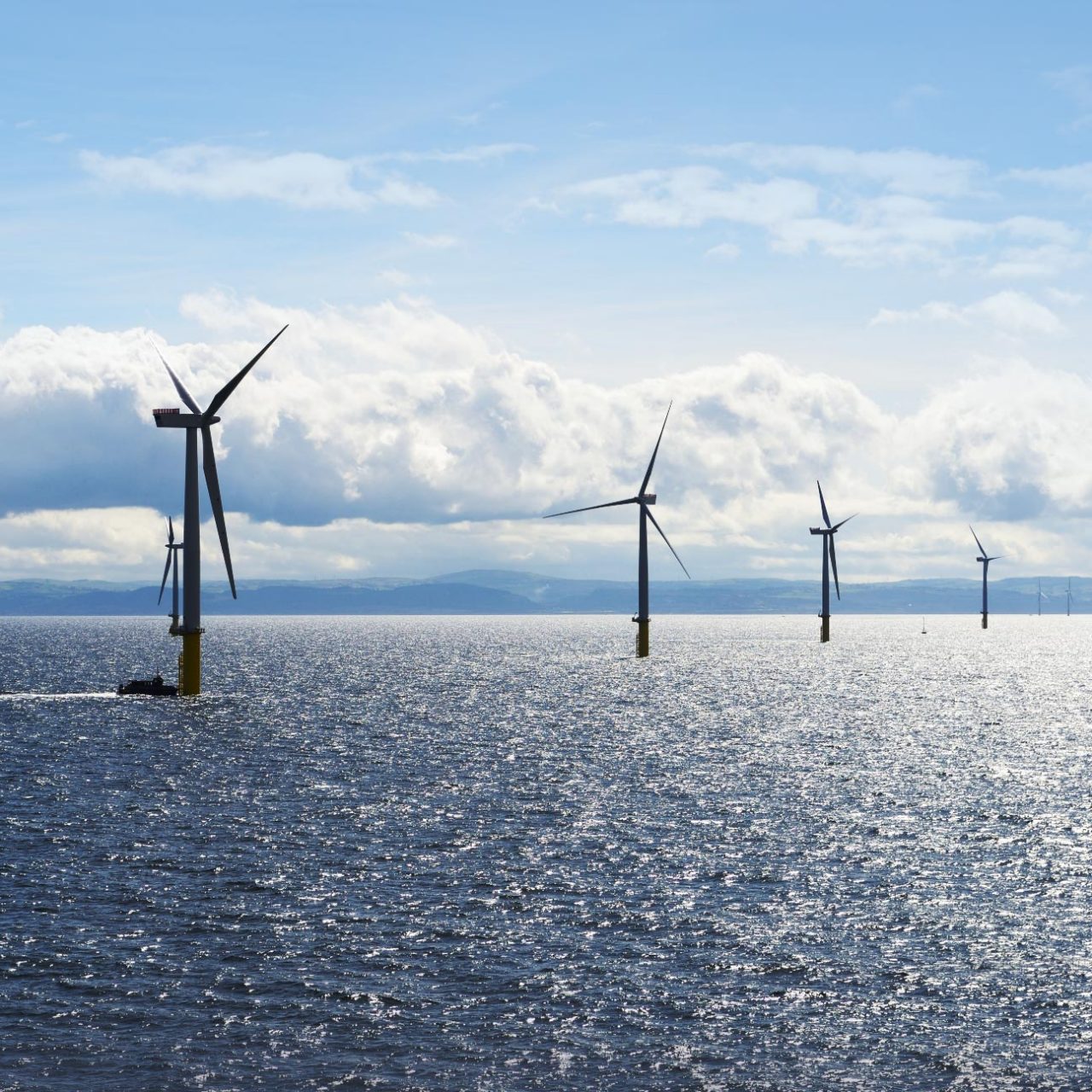 Array of wind turbines and small boat in the sea against blue sky and white clouds