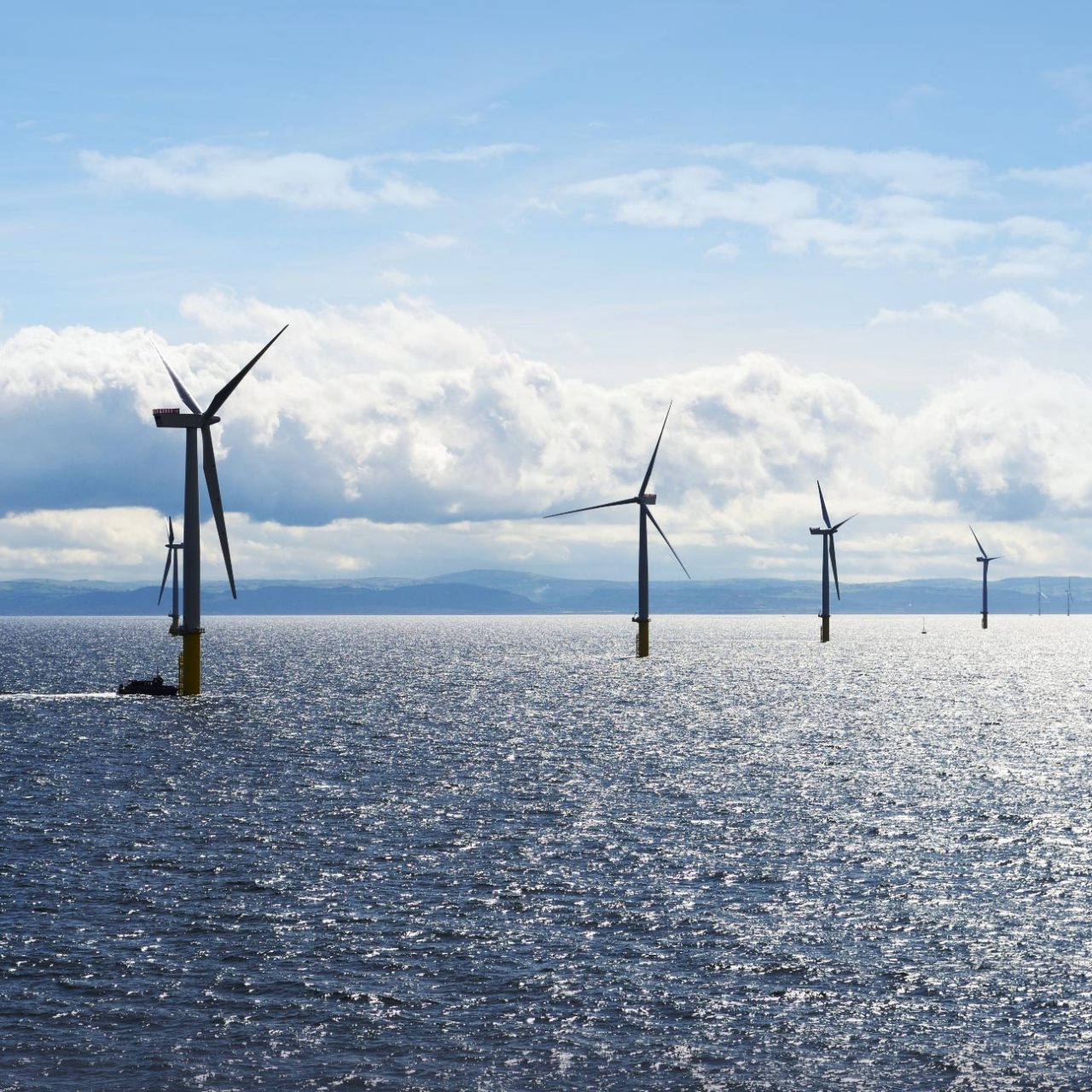 Array of wind turbines and small boat in the sea against blue sky and white clouds