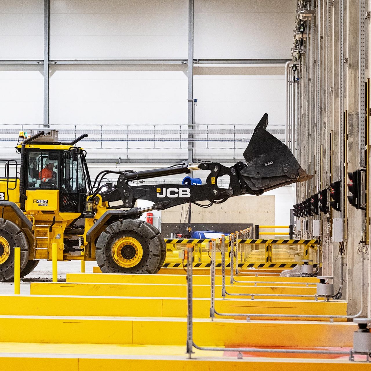 Yellow JCB digger with raised loader bucket with yellow metal bars in foreground