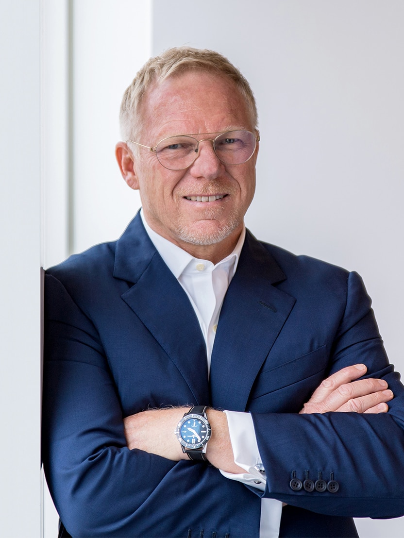 Head and shoulder shot of smiling man with glasses leaning on wall with arms crossed