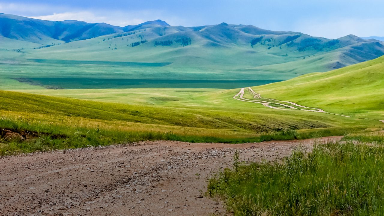 Winding dirt track through lush rolling hills of central Mongolian steppe
