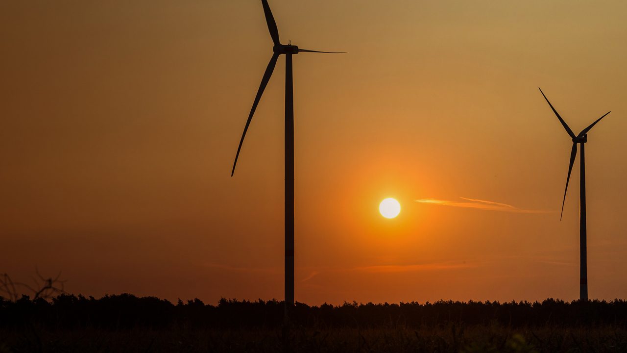 Orange sun sets behind two wind turbines