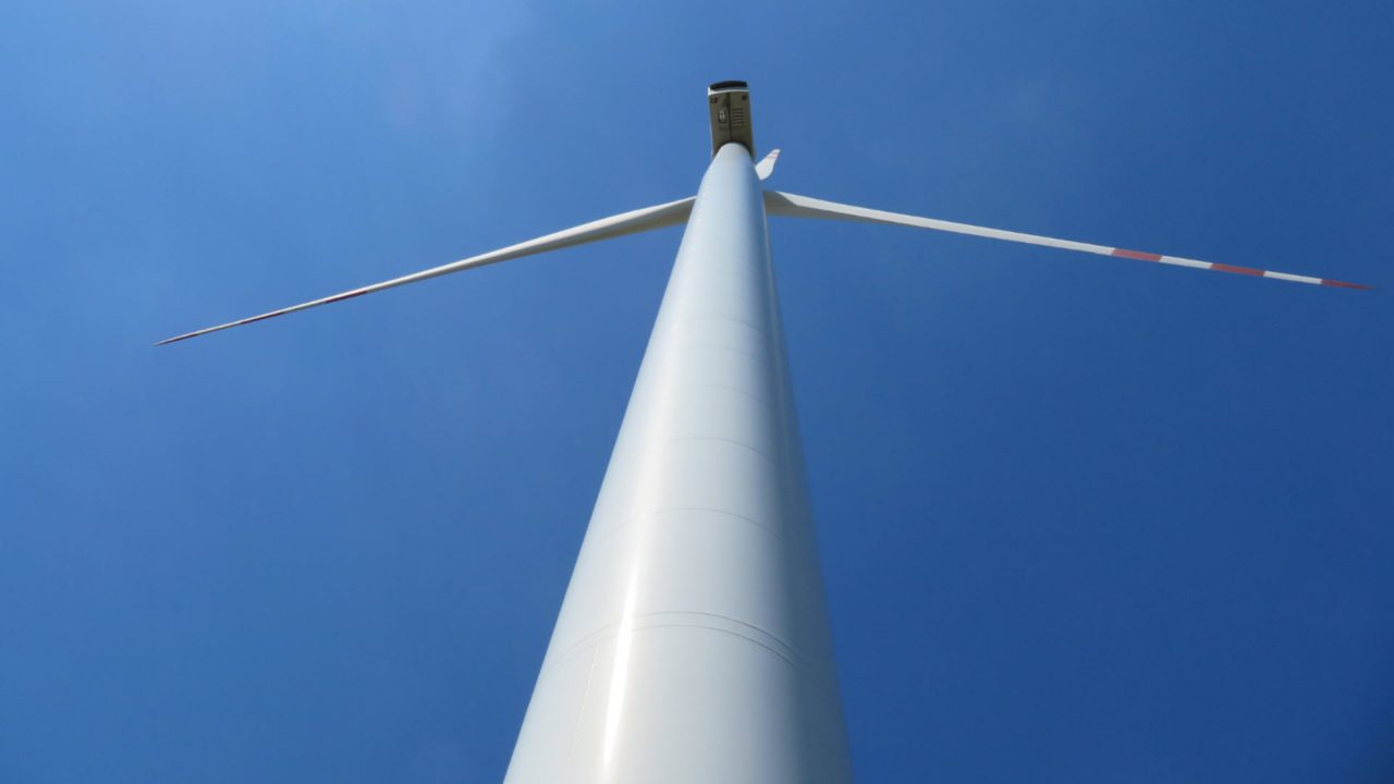 White wind turbine from below with blue sky in the background